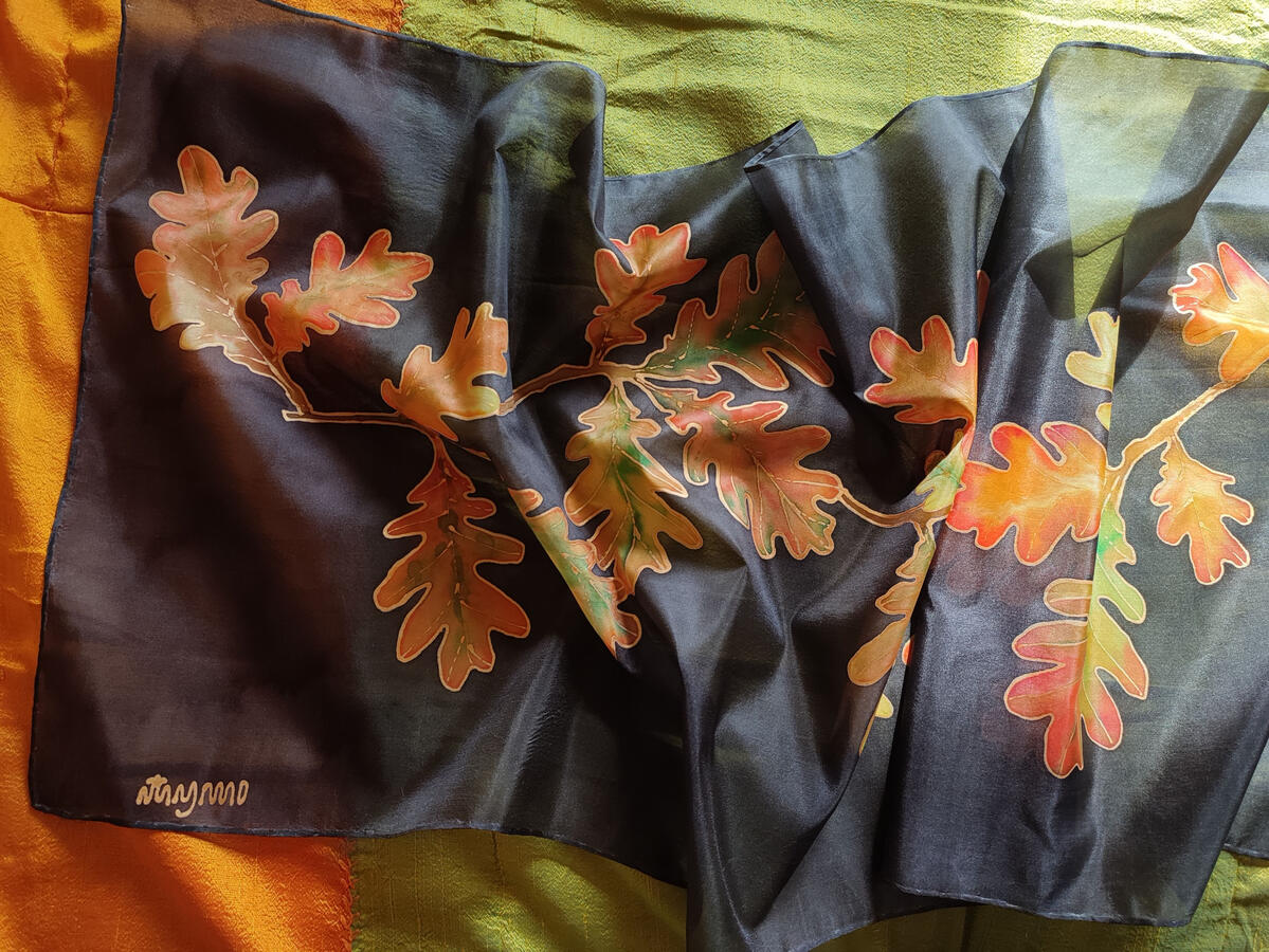 Pañuelo de seda natural pintado a mano con motivo de hojas de robre en tonos anaranjados, verdes y amarillos en un fondo negreo.