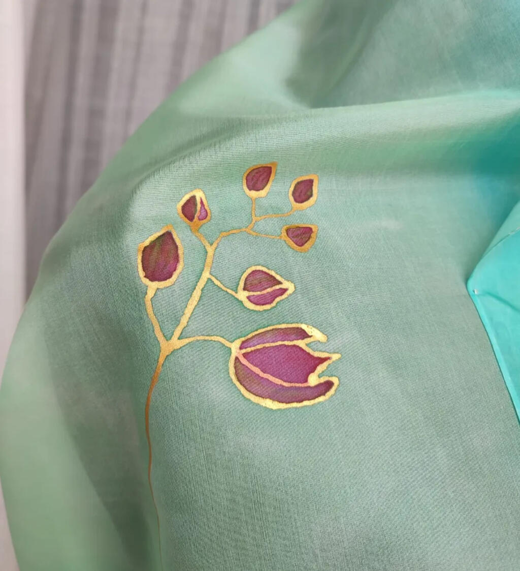 Detalle de pañuelo de seda natural pintado a mano con guta dorada de capullos de flores de orquídea en color púrpura sobre un fondo azul cielo.